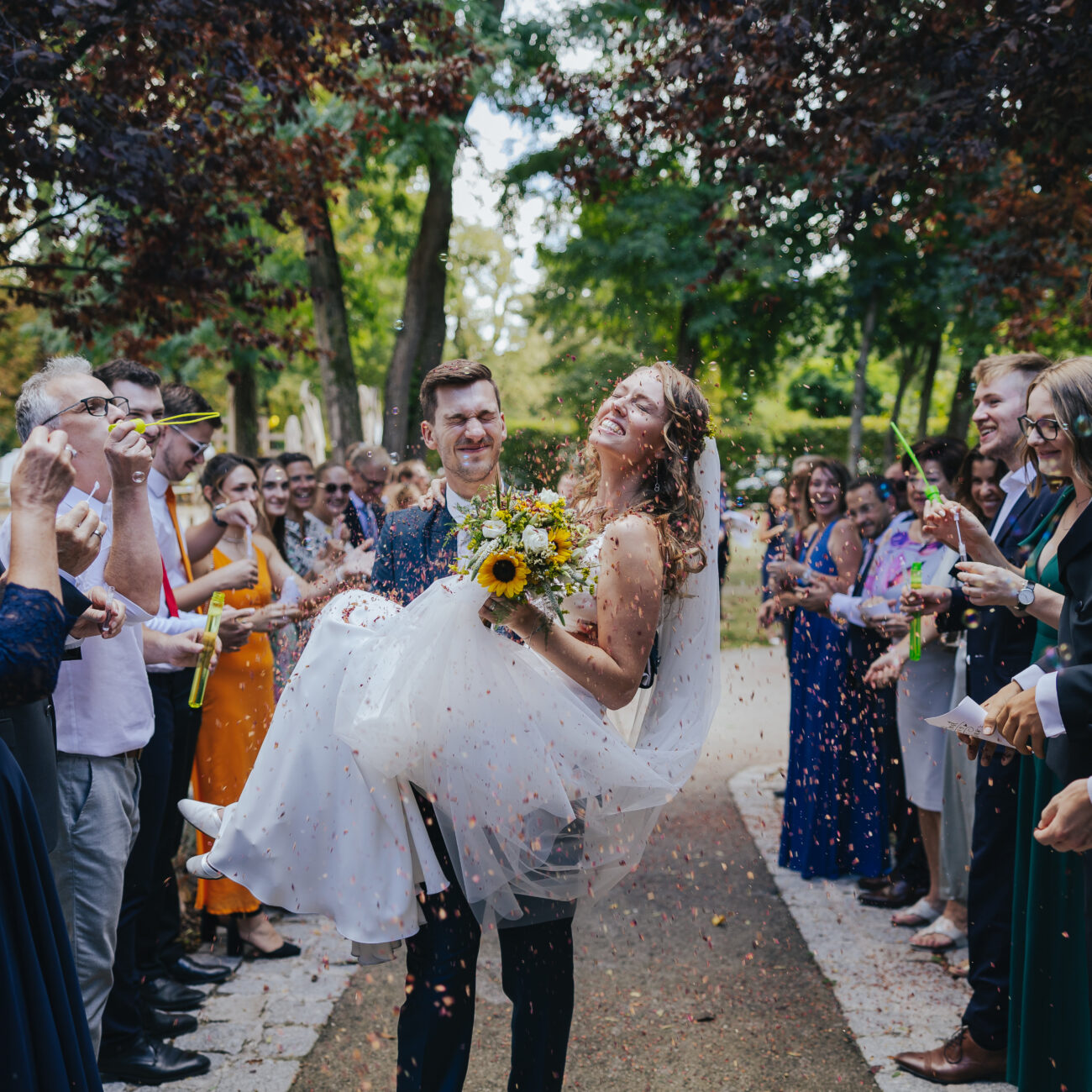 Bräutigam trägt Braut in den Armen durch den Spalier der Gäste